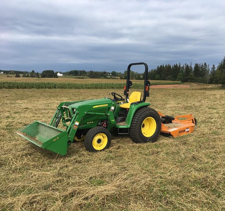 Compact tractor with a rotary cutter mowing a dry field